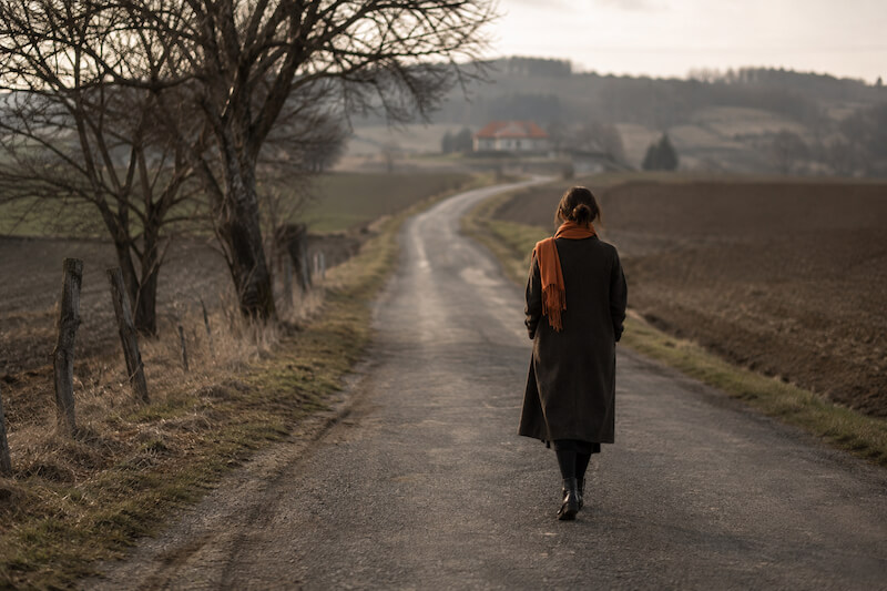 Frau geht allein auf einem ländlichen Weg – Symbolbild für transgenerationale Weitergabe, Erinnerung sowie die Folgen von Flucht und Vertreibung.